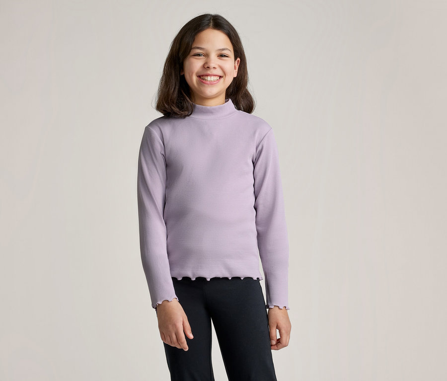 Une fille souriante aux cheveux bruns porte un T-shirt à manches longues violet avec un col roulé et un legging noir sur un fond clair.