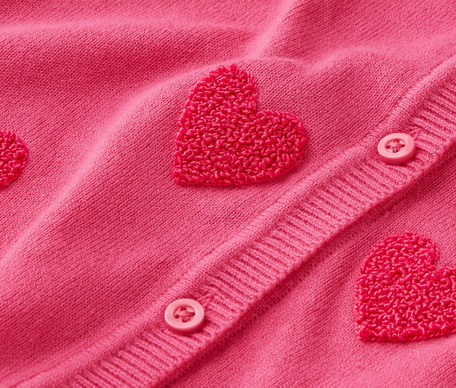 Gros plan sur un cardigan rose avec des applications en forme de cœur et des boutons.