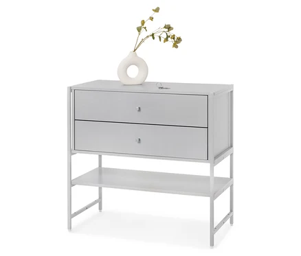 Commode grise à deux tiroirs et une étagère, sur laquelle repose un vase blanc avec des plantes.