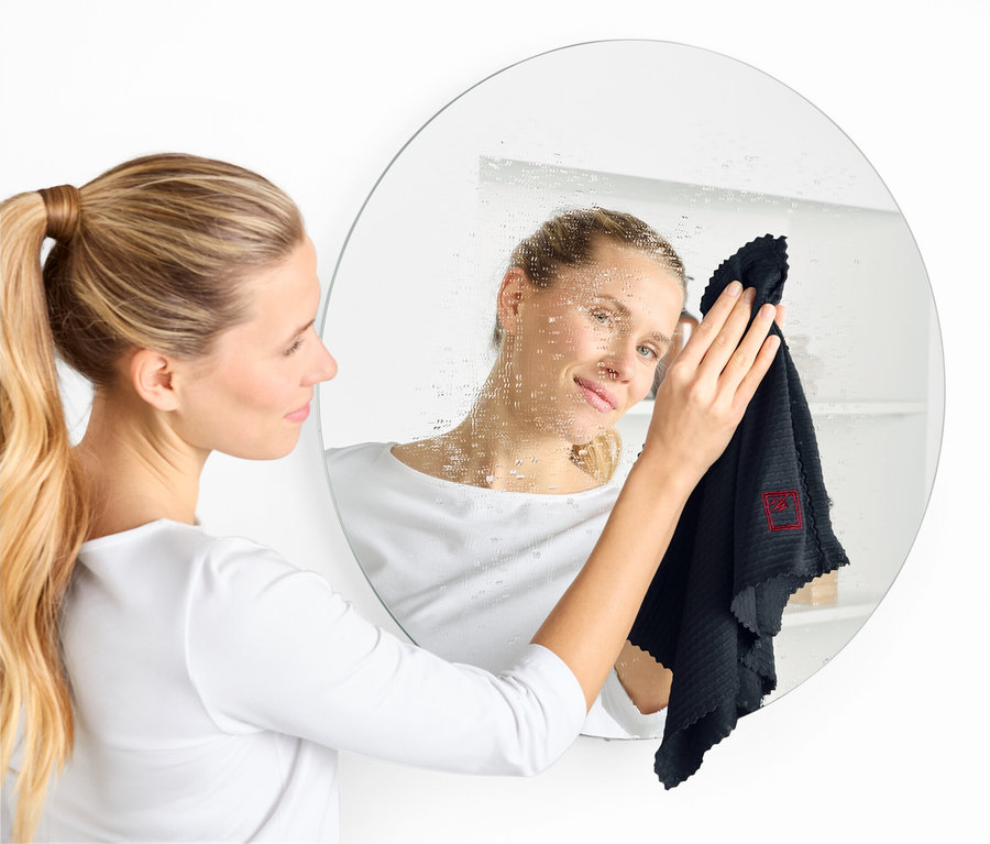 Femme nettoie un miroir rond avec un chiffon noir.