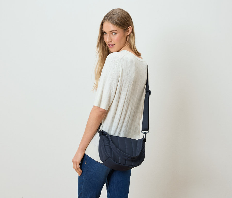 Une femme regarde par-dessus son épaule et porte un sac bandoulière bleu marine.