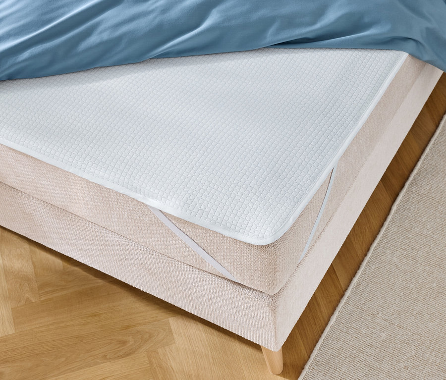 Gros plan d'un lit avec une literie bleue et un protège-matelas blanc avec des bandes élastiques.