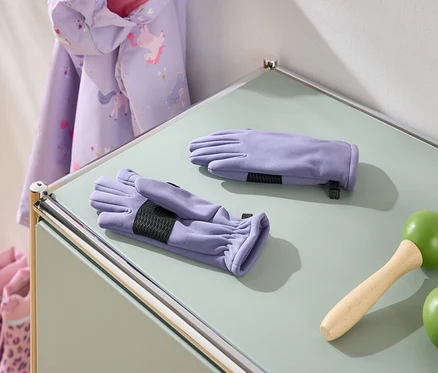 Sur une table, des gants violets, une corde à sauter avec des poignées vertes, une veste à motif de licorne et des bottes roses.