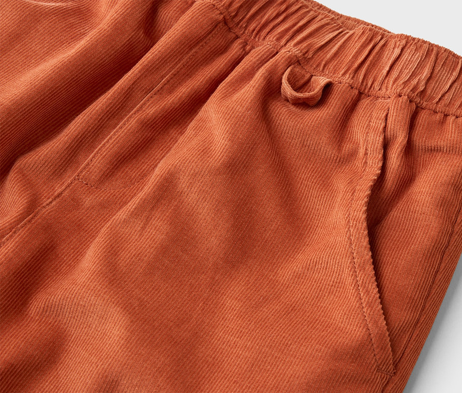 Gros plan sur un pantalon en velours côtelé orange avec une taille élastique et une poche latérale.