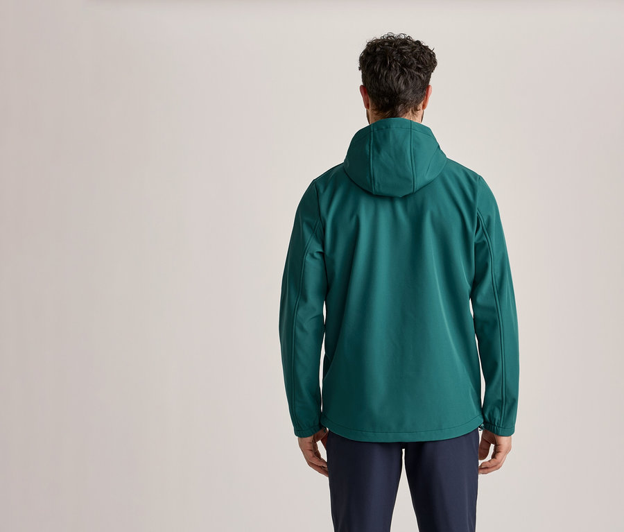 Un homme vu de dos, portant une veste à capuche verte et un pantalon bleu foncé.