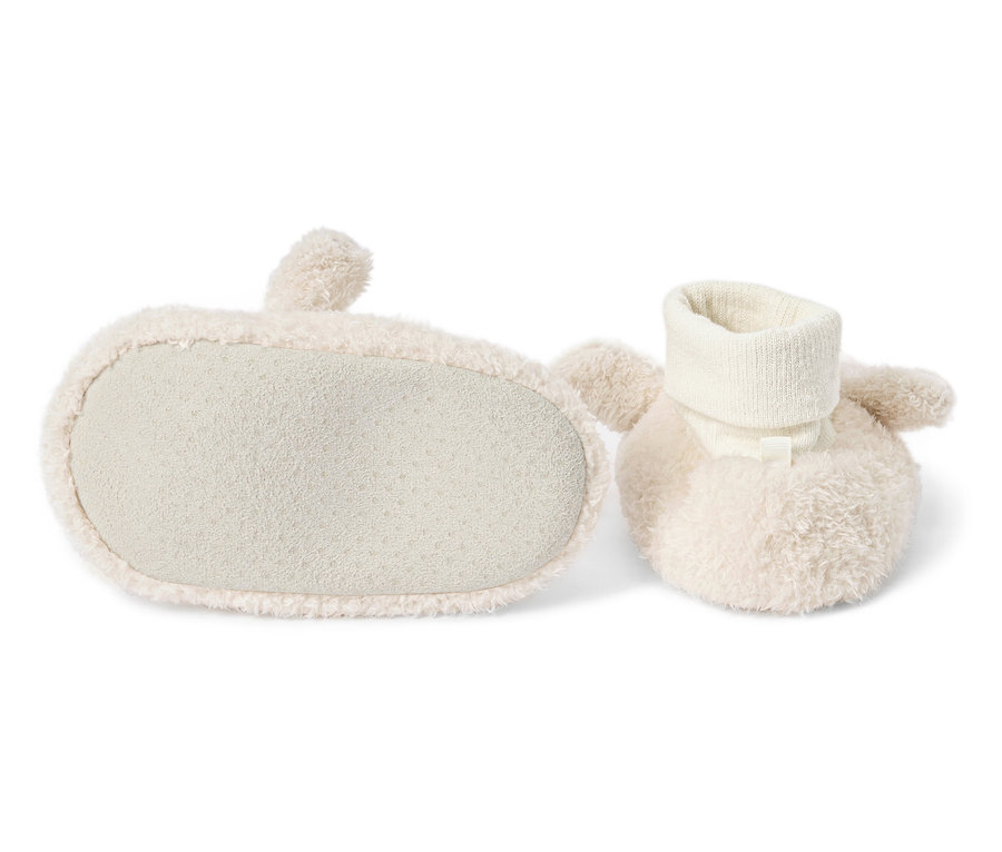 Deux chaussons de bébé couleur crème, dont un avec vue sur la semelle, sont posés sur un fond blanc.