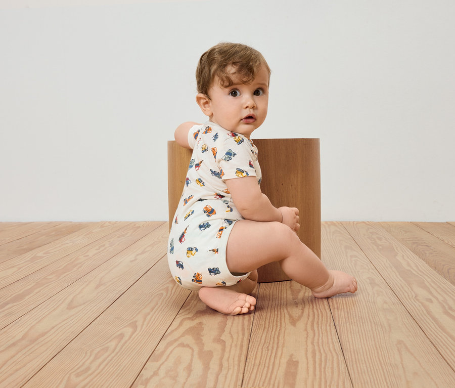 Un bébé est assis sur un plancher en bois et s'appuie contre un tabouret en bois.