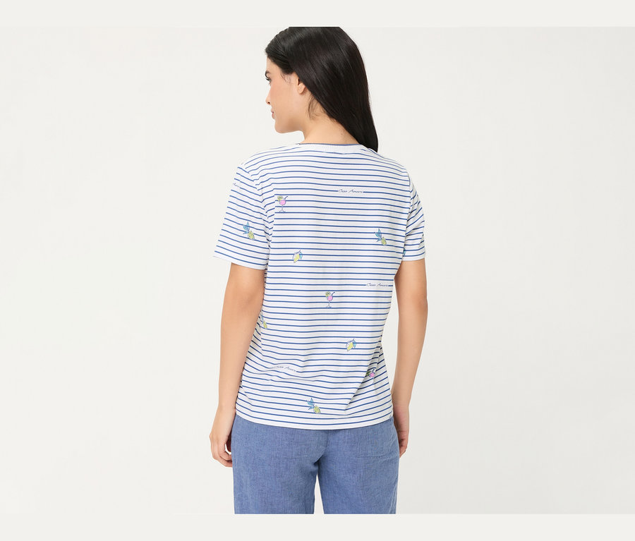 Femme de dos, portant un T-shirt Olsen rayé blanc et bleu avec des motifs de cocktails et de citrons, et un pantalon bleu.