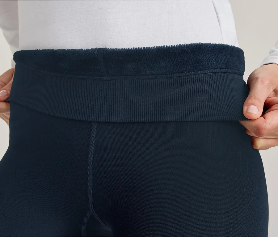 Des mains tirent la ceinture côtelée d'un legging bleu foncé, révélant la doublure polaire marine moelleuse à l'intérieur.