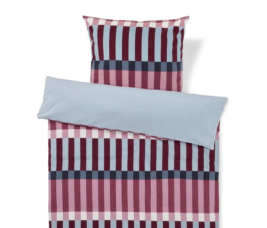 Une parure de lit rayée bordeaux, bleu clair, bleu foncé et blanc, avec un drap uni bleu clair plié sur le dessus.