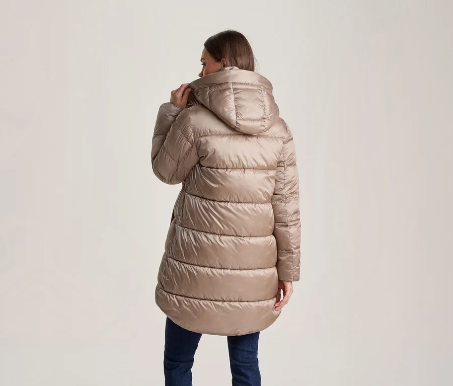 Femme vue de dos, portant une doudoune à capuche matelassée beige clair et un jean bleu foncé. Elle tient le col de la veste avec sa main droite.
