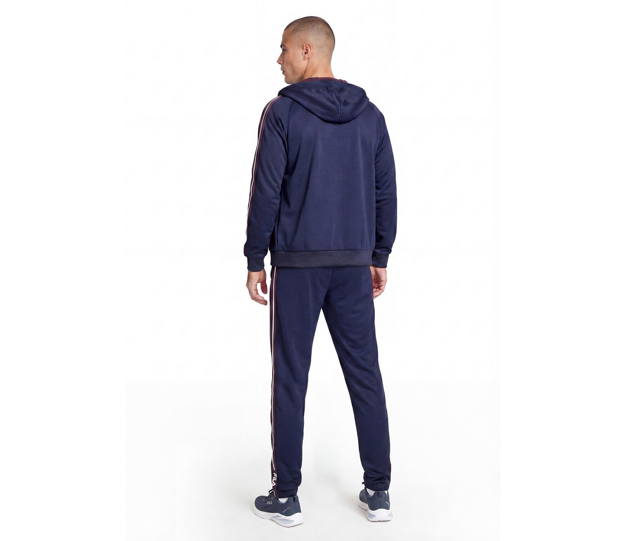 Homme vu de dos portant un survêtement bleu marine avec des rayures rouges et blanches sur les manches et les côtés du pantalon, et des baskets foncées.