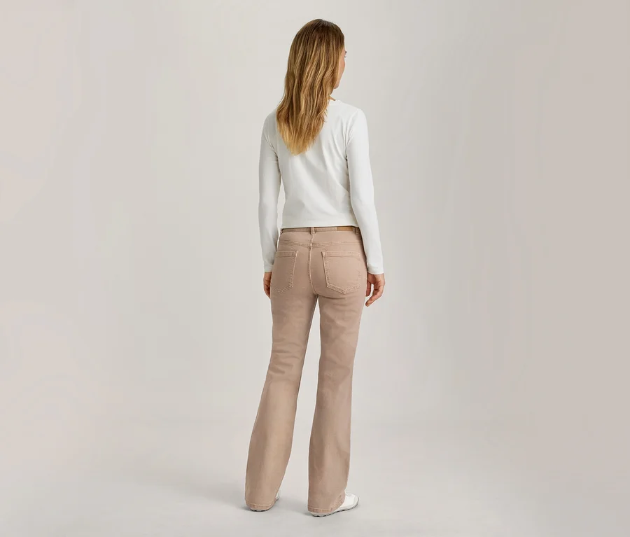 Femme debout de dos, portant un haut blanc à manches longues et un jean évasé marron clair.