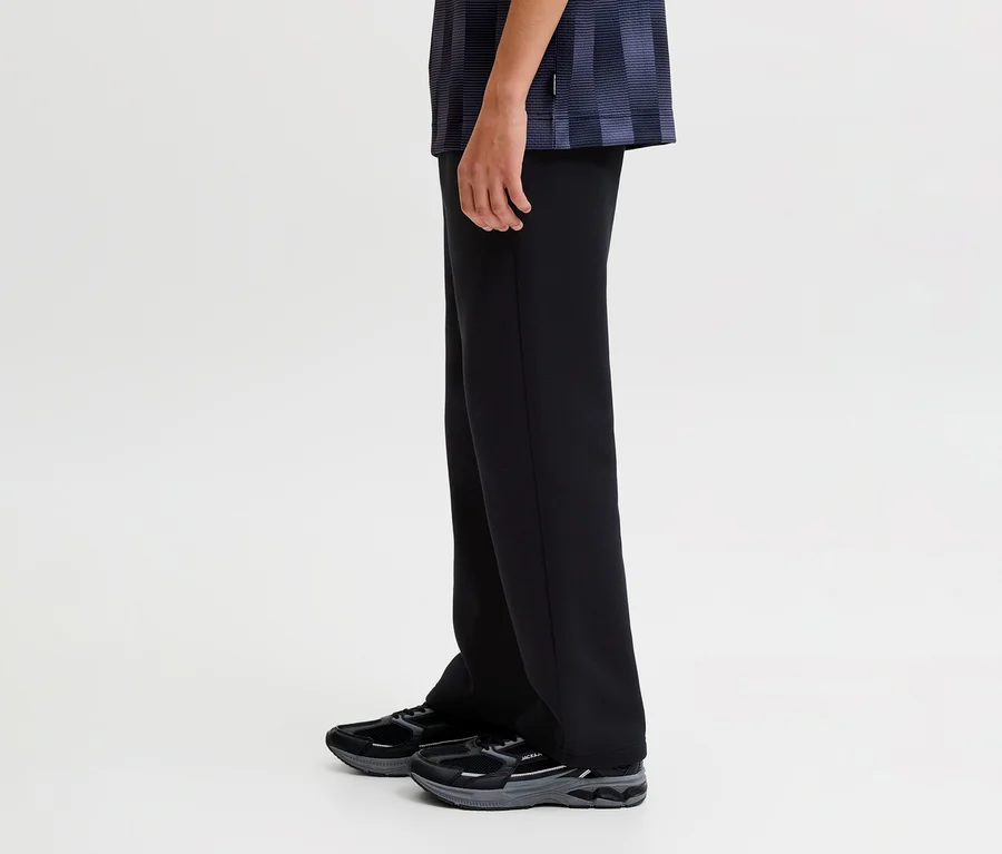 Bas du corps d'une personne portant un pantalon de survêtement noir Jack&Jones Bradley et des baskets noires, debout de profil.