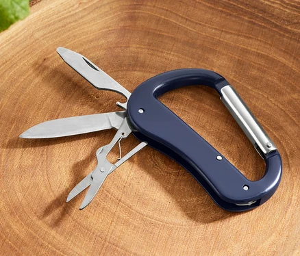 Un mousqueton avec outils polyvalents 5 en 1 avec couteau, scie et ciseaux posé sur une souche d'arbre.