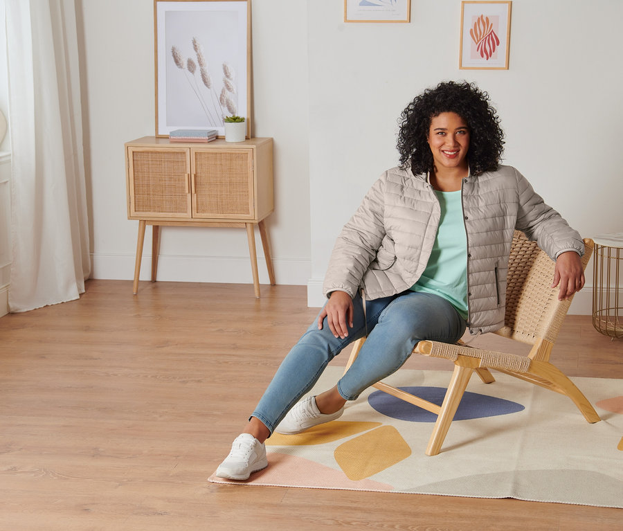 Une femme est assise sur une chaise et porte un t-shirt manches 3/4 menthe, un tregging, des baskets en cuir velours et une veste matelassée à capuche.
