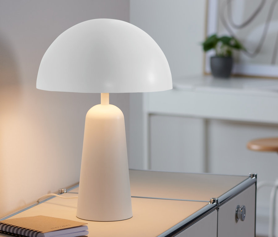 Une lampe de chevet blanche champignon est posée sur une armoire à côté d'un carnet.