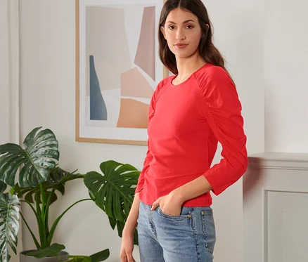 Femme posant en t-shirt rouge manches 3/4 et jean bleu.