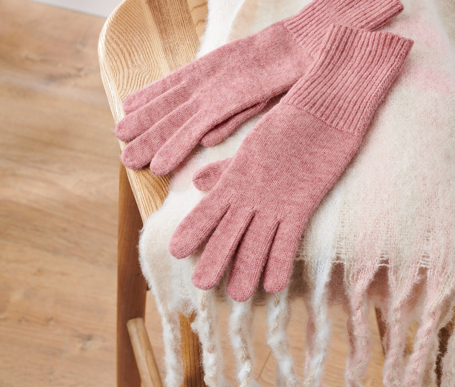 Des gants en maille avec de la laine, rose, sont posés sur une chaise en bois avec un châle blanc.