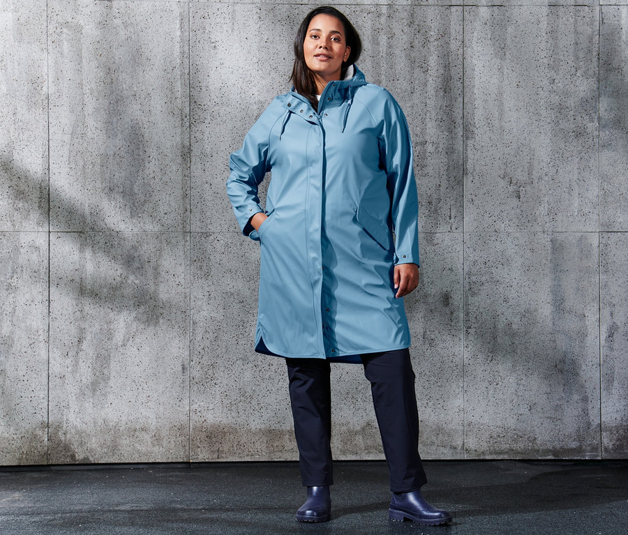Une femme debout portant une parka de pluie « ciré » bleu clair et un pantalon de jogging softshell bleu foncé.