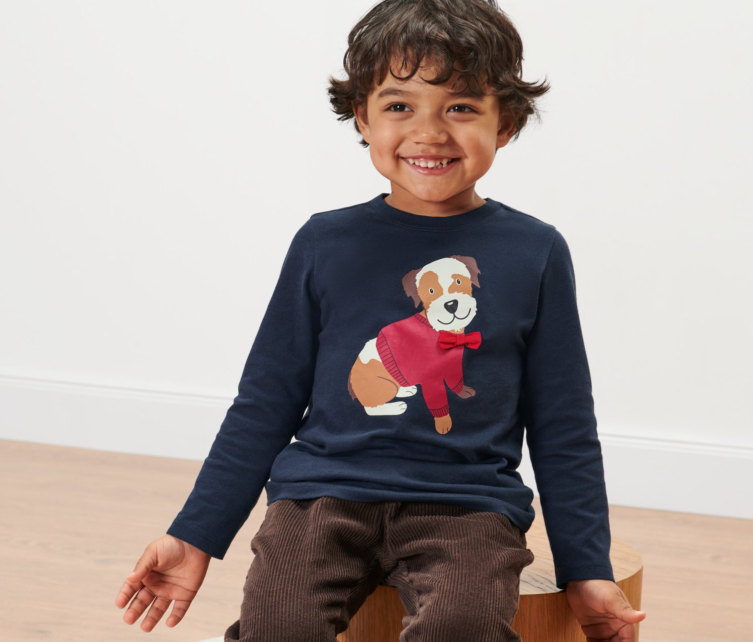 Un garçon souriant est assis et porte un t-shirt manches longues pour tout-petits avec un motif de chien.