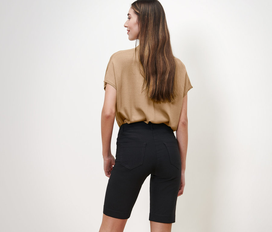 Une femme, vue de dos, porte un chemisier beige et un bermuda en bengaline noir.