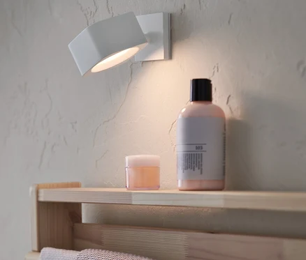 Un éclairage mural à LED avec batterie est fixé au mur. Des produits cosmétiques sont posés sur une étagère en dessous.