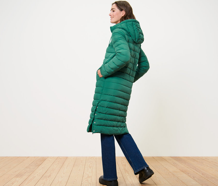 Femme posant de profil dans un long manteau matelassé à capuche.