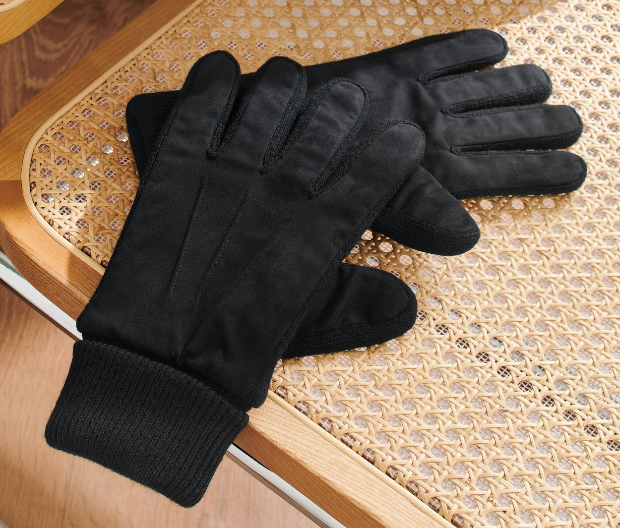 Des gants noirs sont posés sur une chaise en rotin, sur laquelle est posée une veste verte.