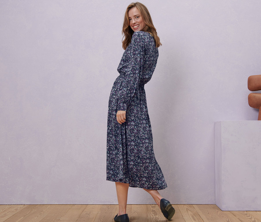 Femme souriant par-dessus son épaule et posant dans une robe midi à imprimé floral.