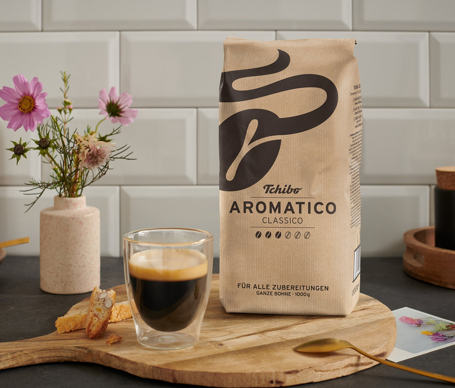 Une tasse de café est posée à côté d'un paquet d'Aromatico Classico - 1 kg Ganze Bohne sur une table en bois.