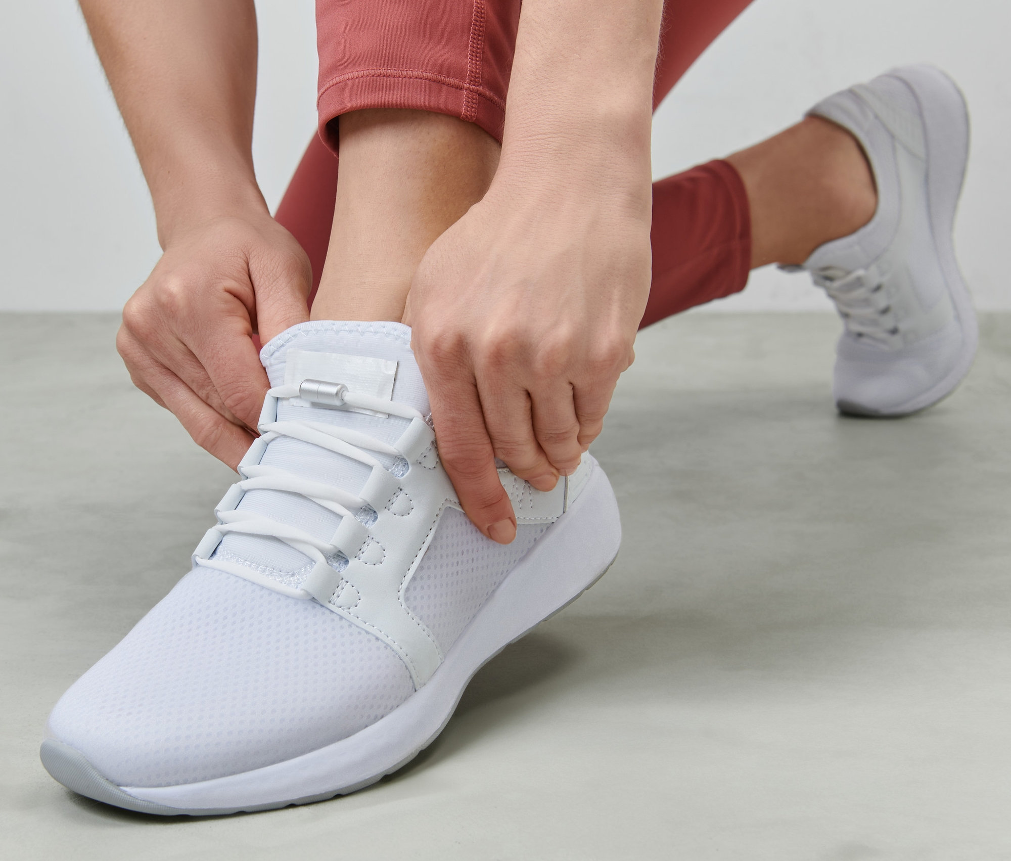 Femme nouant des lacets élastiques sur une chaussure blanche.