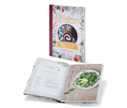 Deux livres de cuisine sur le thème de Noël. Un livre est fermé et se tient verticalement, l'autre est ouvert et repose horizontalement. On peut voir le livre « Christmas is a feeling » (en allemand).