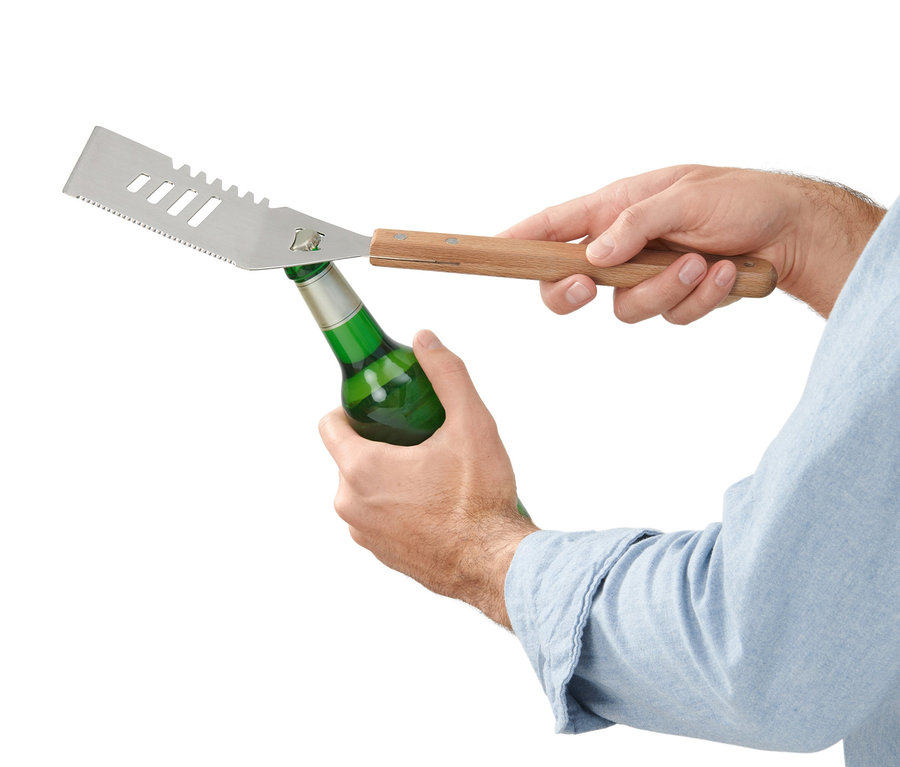 Un homme ouvre une bouteille verte avec un outil polyvalent pour barbecue.