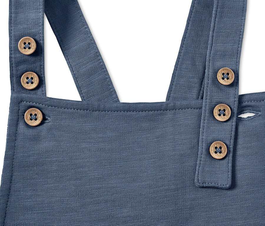 Gros plan sur une salopette bleue pour bébé avec des boutons en bois.