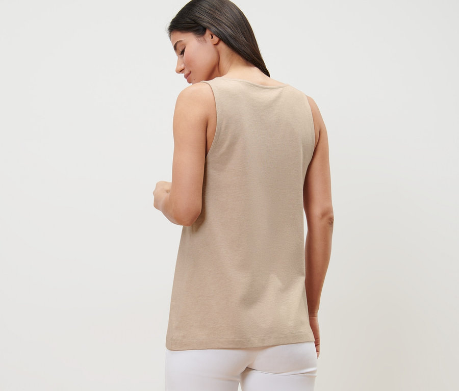 Une femme, vue de dos, porte un haut beige chiné avec patte de boutonnage et un pantalon blanc.