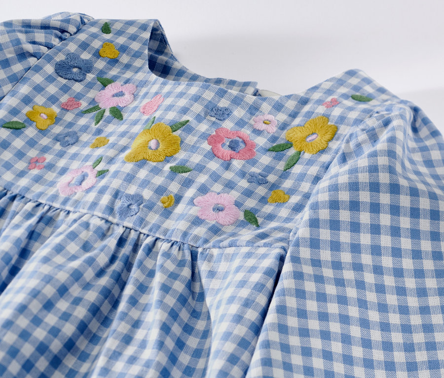Gros plan sur une robe tissée pour enfant à carreaux bleu et blanc avec des broderies florales.