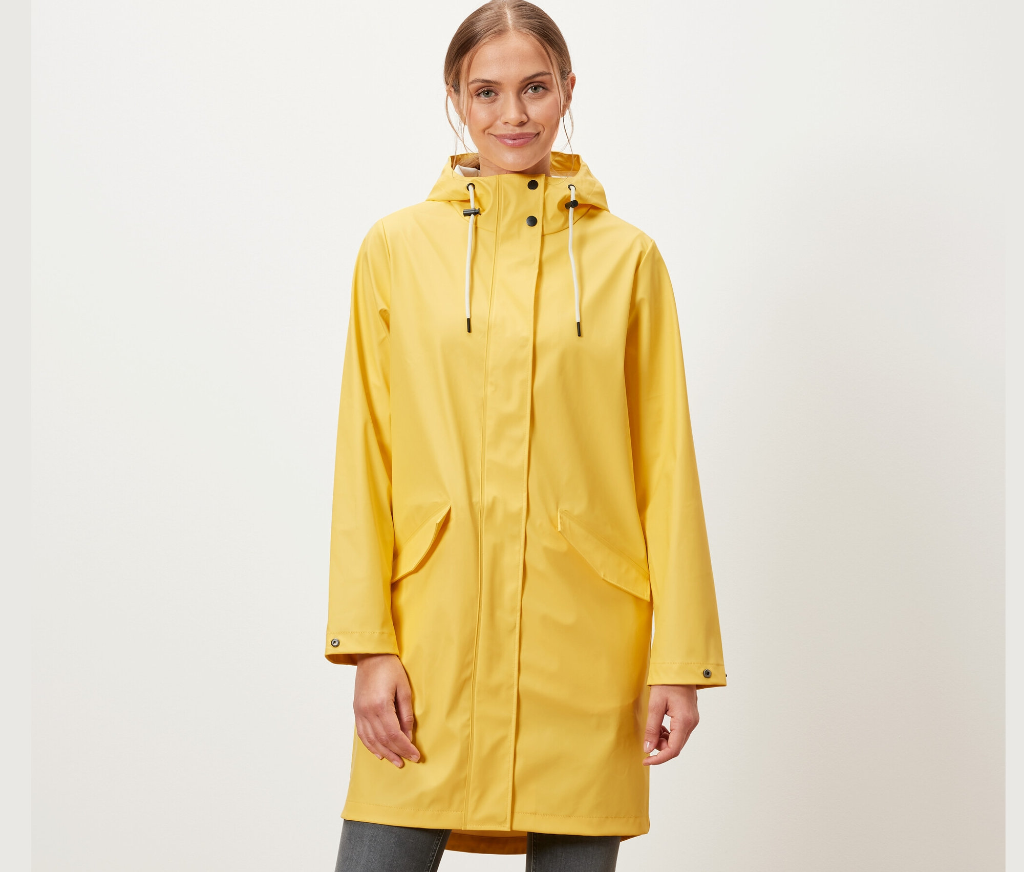 Une femme porte une parka de pluie jaune « ciré » et un jean gris.