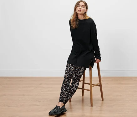 Une femme est assise sur un tabouret et porte une robe noire et un legging à motif intégral.