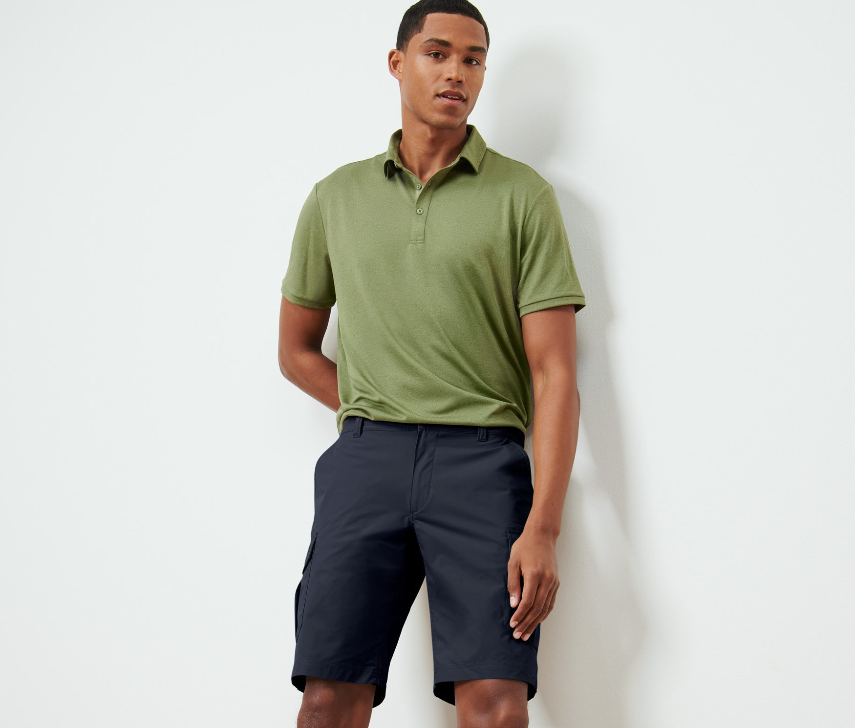 Un homme debout portant un polo olive et un short fonctionnel bleu foncé.
