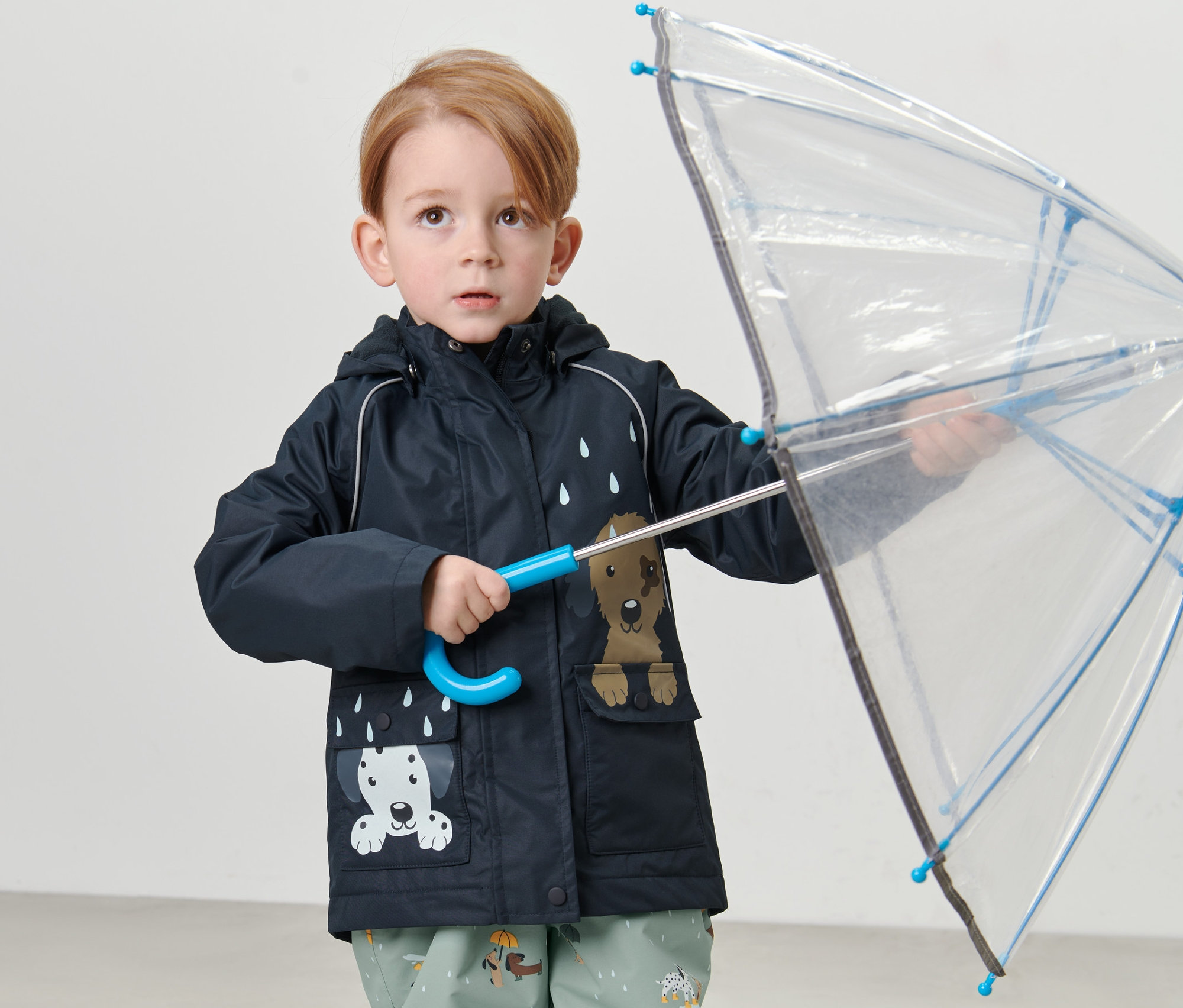 Un garçon tient un parapluie transparent et porte une veste de pluie thermique pour enfant, chien.