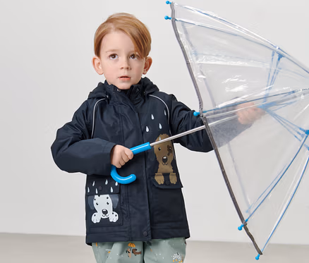 Un garçon tient un parapluie transparent et porte une veste de pluie thermique pour enfant, chien.