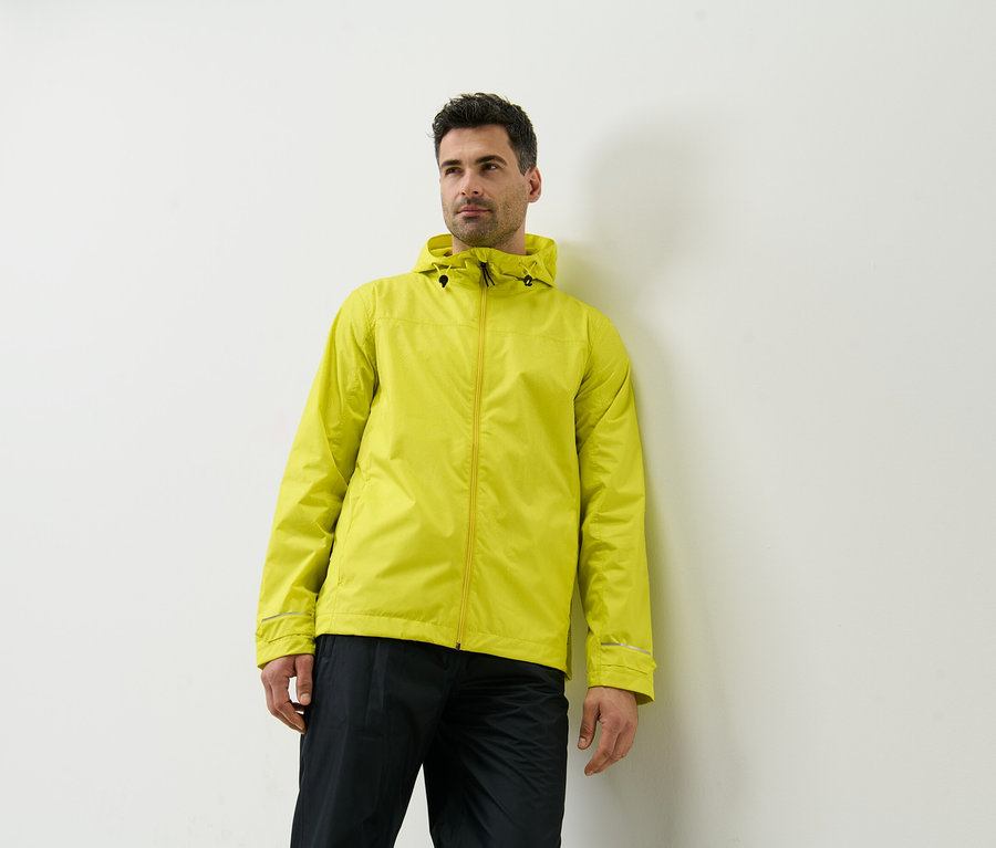 Un homme appuyé contre un mur portant une veste de pluie jaune.