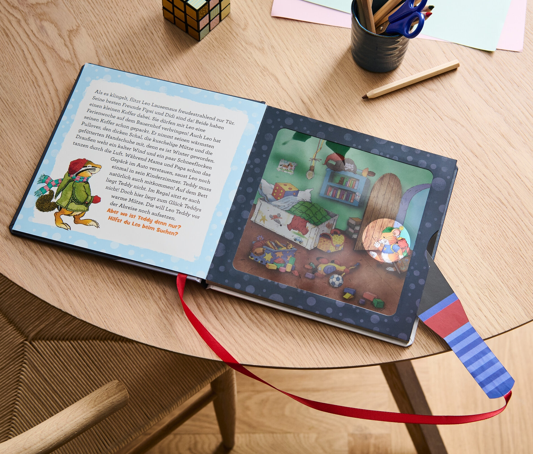 Le livre «
on Leo Lausemaus – mein Taschenlampenbuch
on » est ouvert sur une table à côté de crayons de couleur et d'un cube.