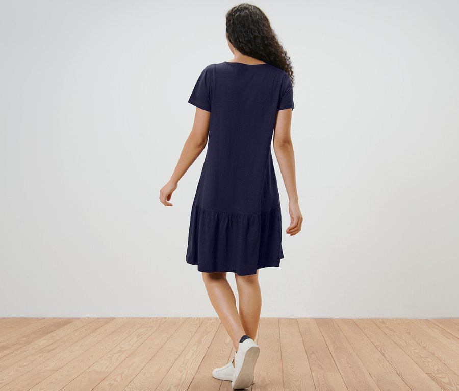Femme vue de dos portant une robe en jersey à volants bleu foncé.