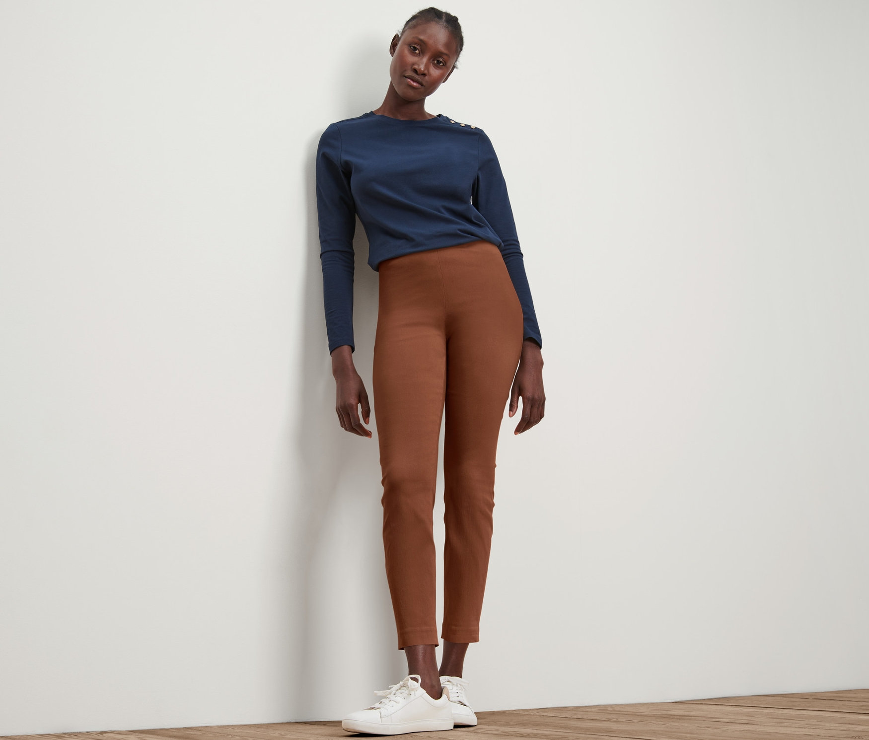Une femme pose en pantalon stretch cognac et haut bleu.