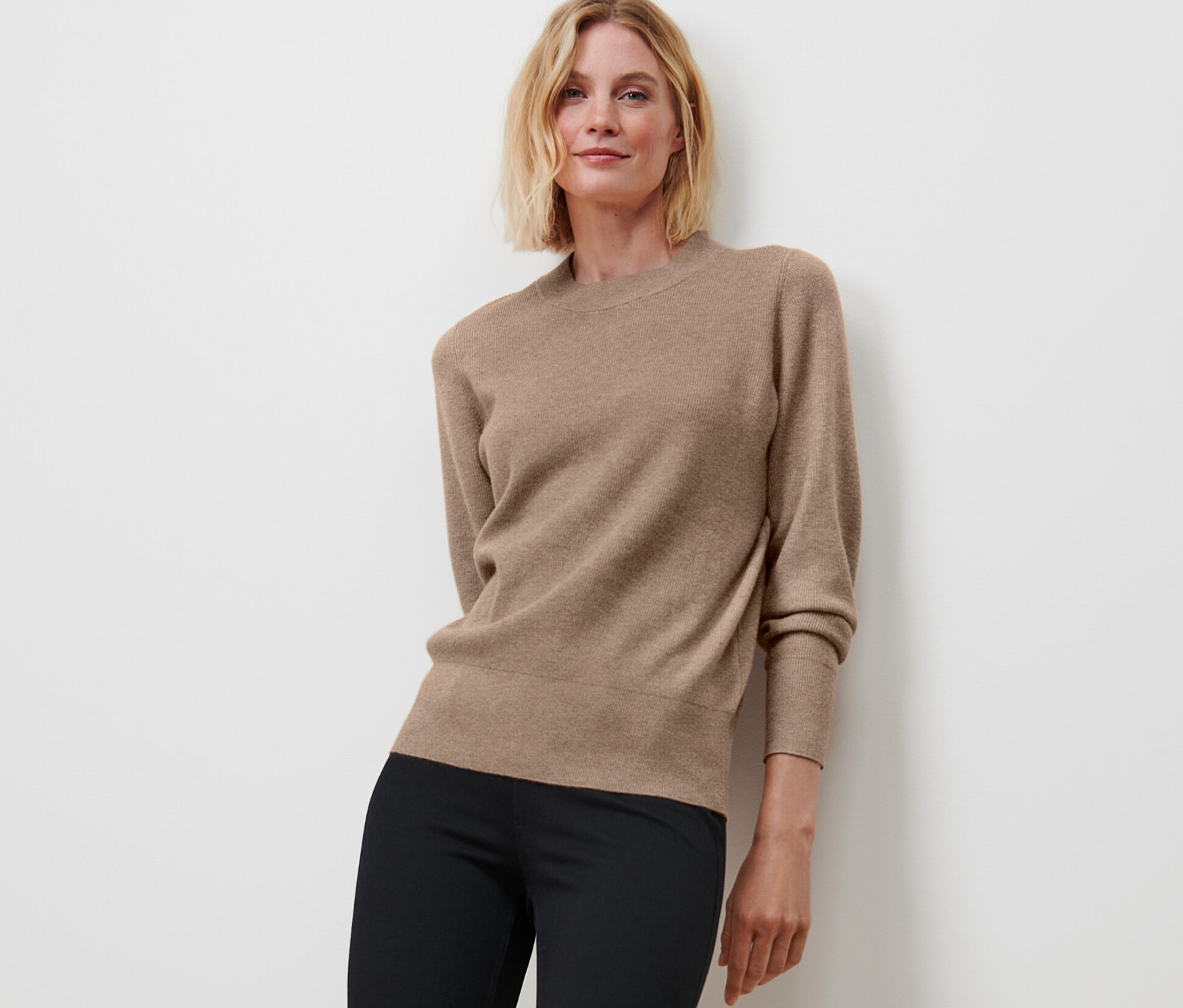 Femme posant en pull en maille fine beige chiné et pantalon noir.