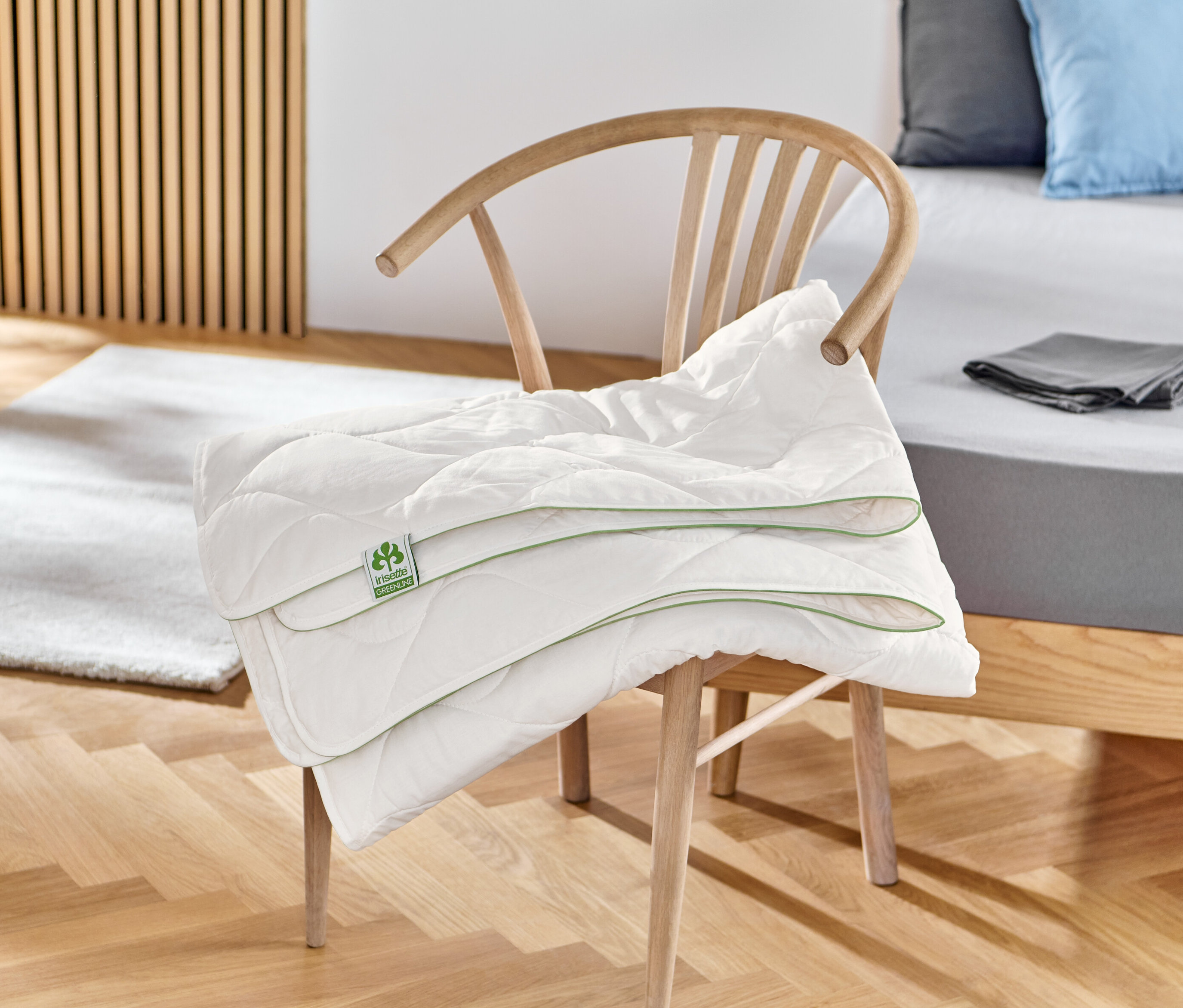 Une couette en coton irisette® greenline blanche pliée est posée sur une chaise en bois.