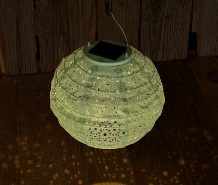 Un lampion solaire suspendu avec des trous décoratifs projette de la lumière sur un plancher en bois.