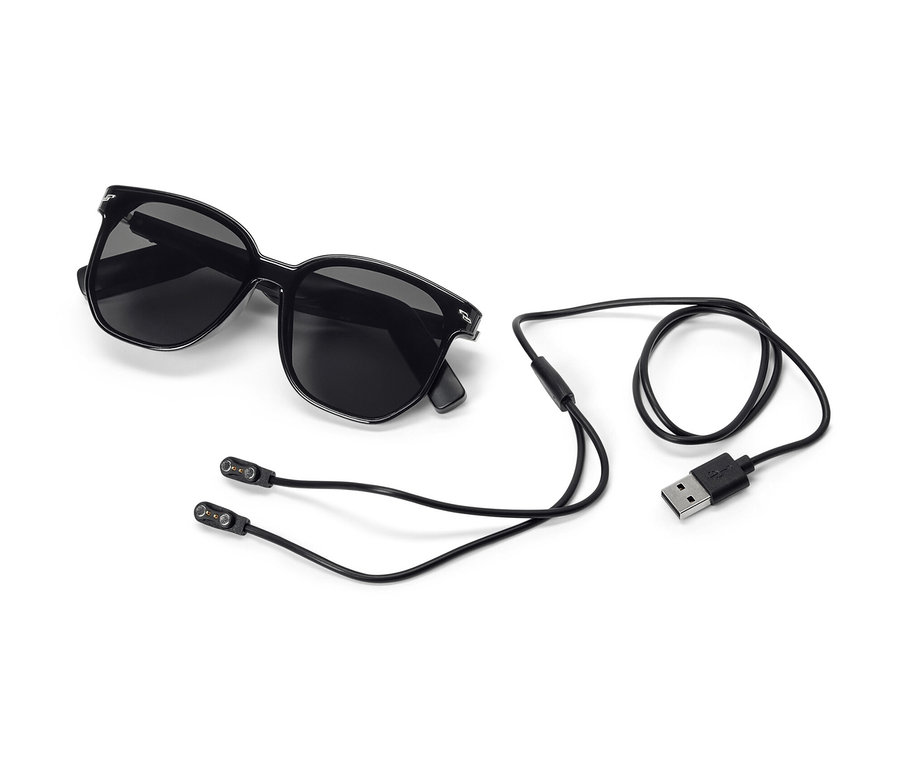 Lunettes de soleil noires avec écouteurs Bluetooth® et câble de chargement sur fond blanc.